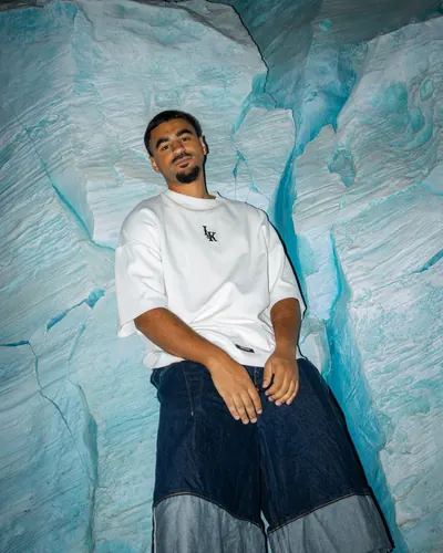 Barros leans into a turquoise ice-blue rock face, flash-lit in an oversized white tee and denim.