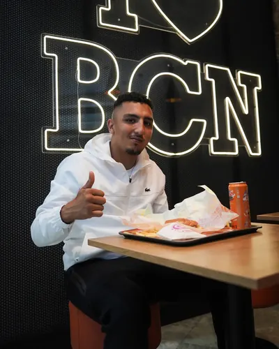 Morad gives a thumbs-up over his tray, framed by the illuminated BCN letters.